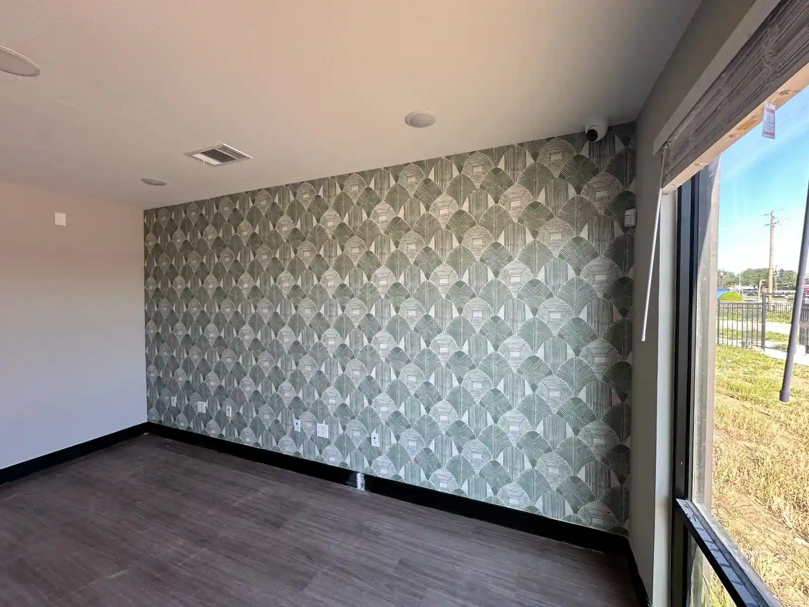 Sunlit room with a full gray Art Deco fan-pattern wallpaper feature wall beside tall windows.