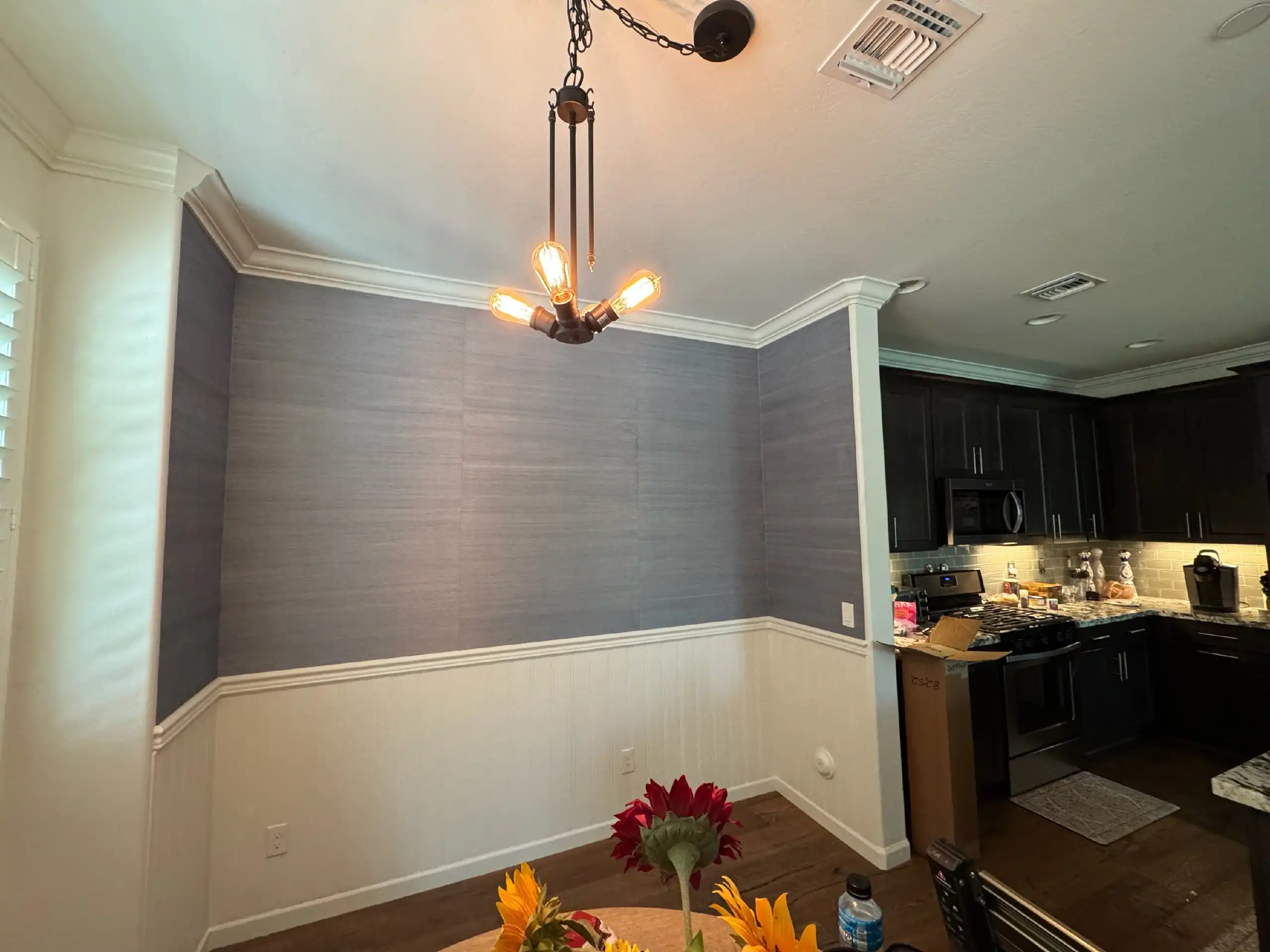 Blue-gray textured wallpaper above white wainscoting in an open dining area.