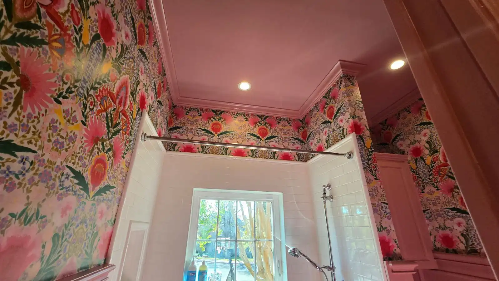 Bathroom with large multicolor floral wallpaper, a rosy pink ceiling, and white tile around the shower.