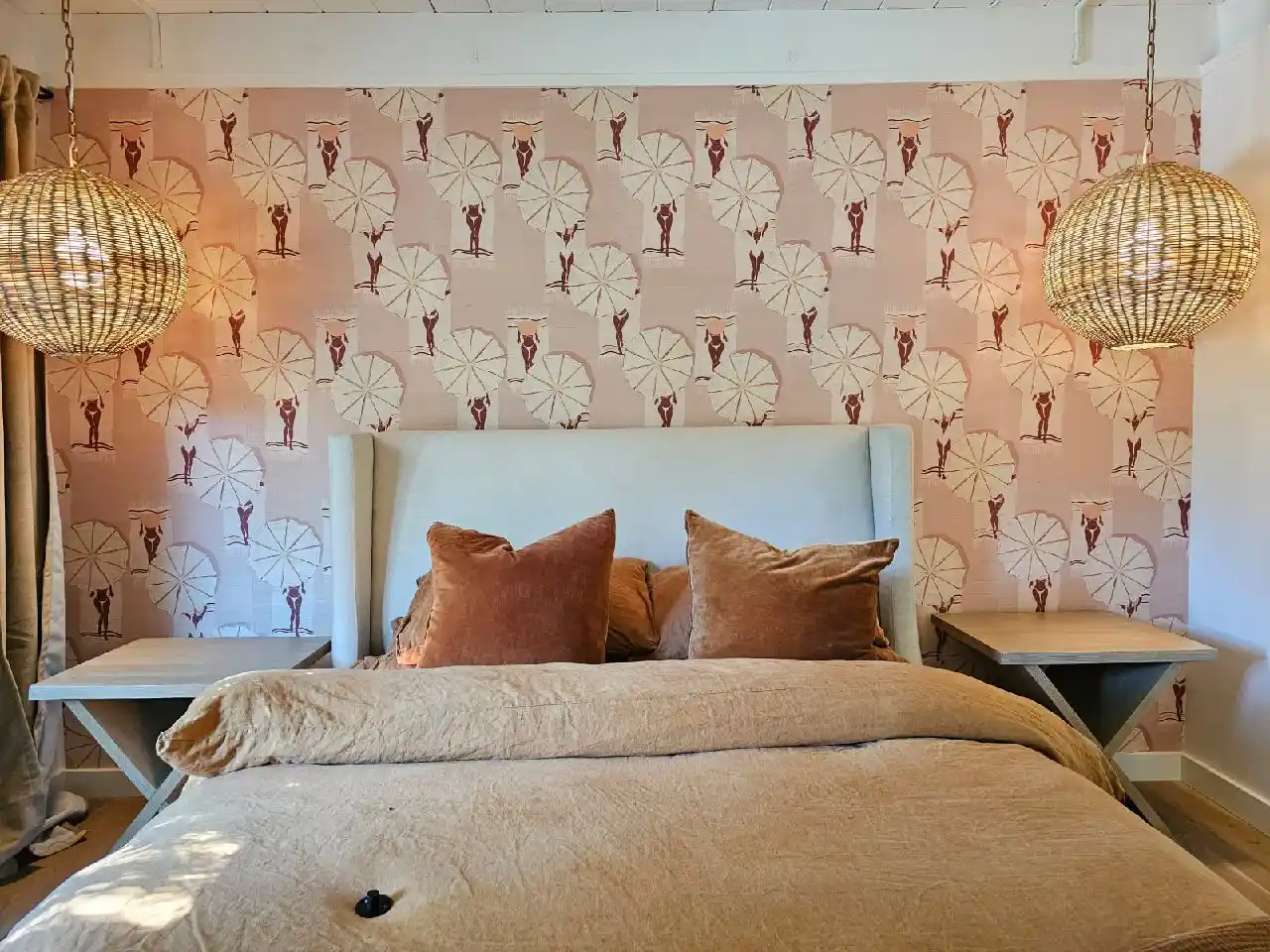 Bedroom with peach wallpaper in a repeating white parasol pattern behind a neatly made bed.